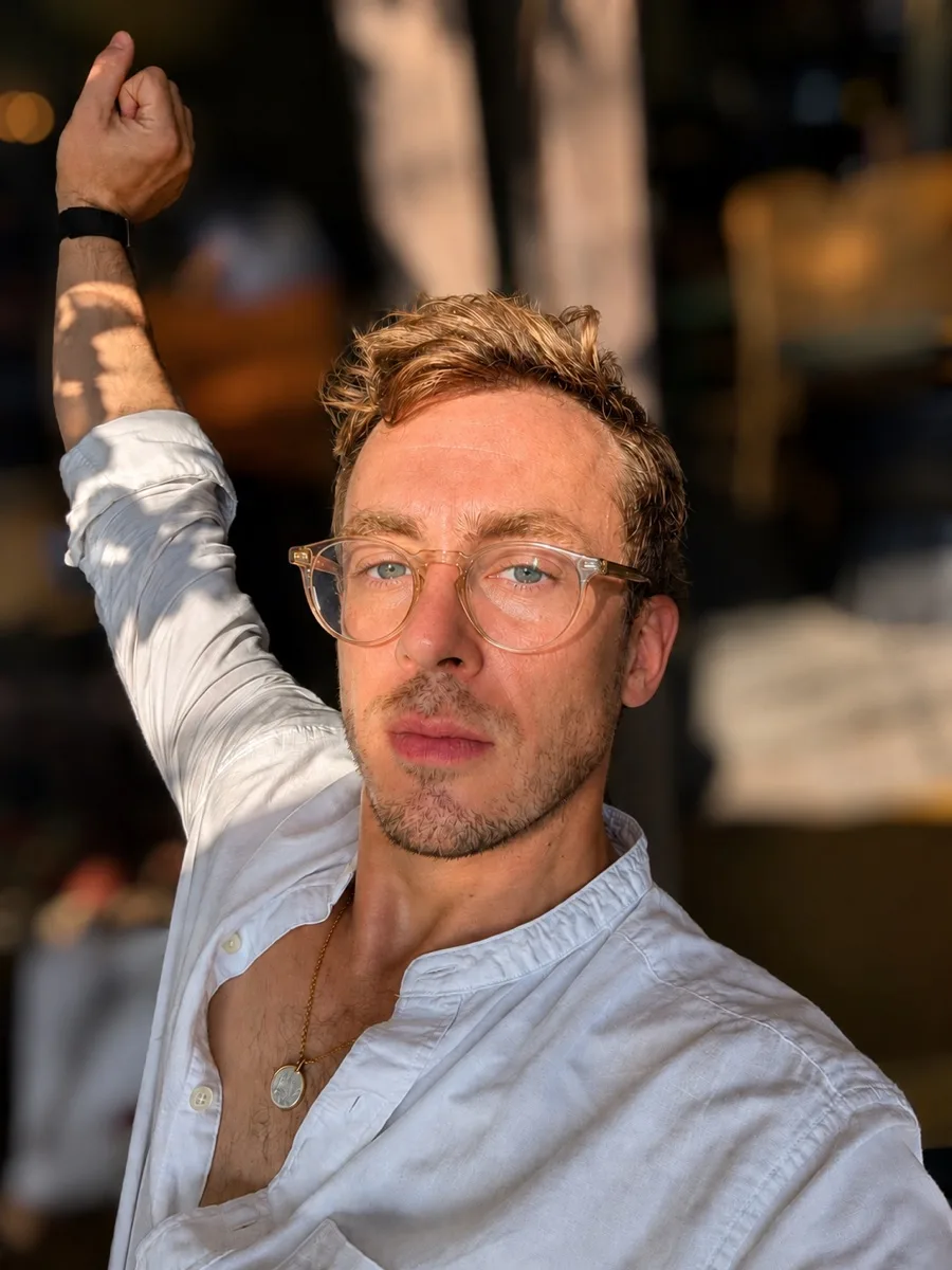 Hermes, in a white linen shirt and clear glasses, one arm raised, in warm late light